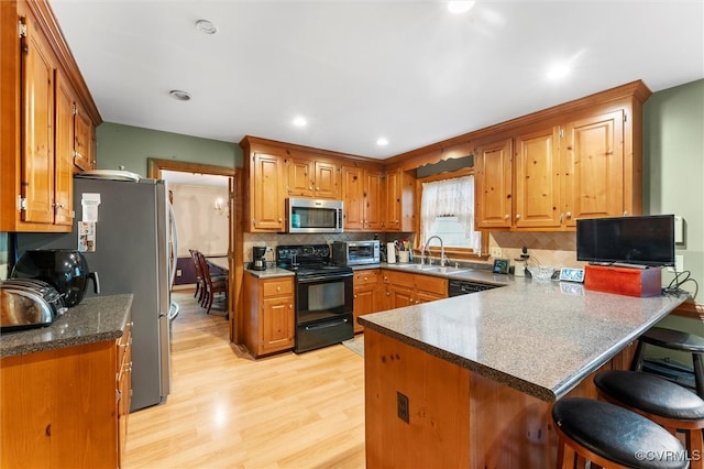 kitchen featuring black appliances, a sink, a peninsula, light wood-style floors, and decorative backsplash