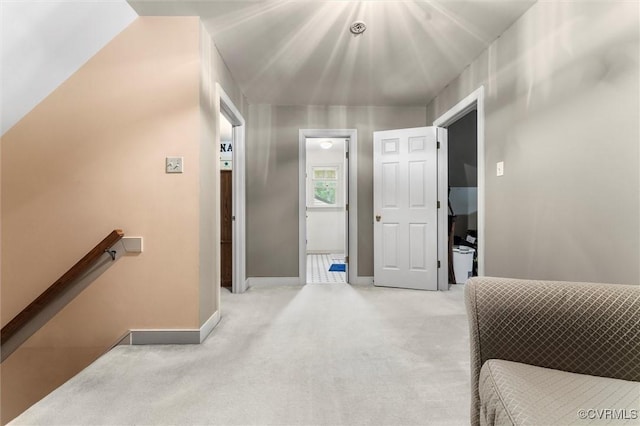 hall with an upstairs landing, light carpet, and baseboards