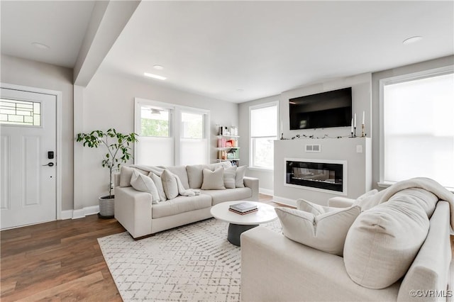 living area featuring recessed lighting, baseboards, a glass covered fireplace, and wood finished floors