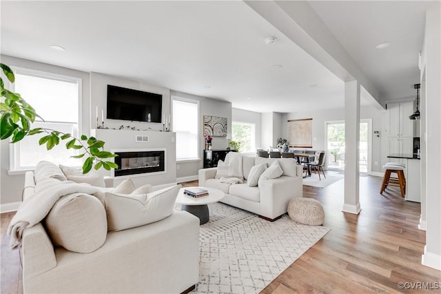 living room with a glass covered fireplace, recessed lighting, baseboards, light wood-type flooring, and visible vents