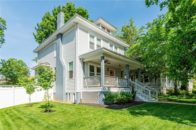 american foursquare style home featuring a porch, ceiling fan, a chimney, a front yard, and fence
