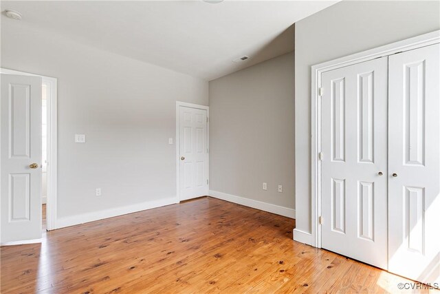 unfurnished bedroom featuring baseboards, light wood finished floors, visible vents, and a closet