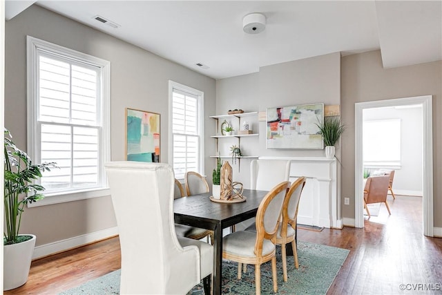 dining space featuring baseboards, wood finished floors, visible vents, and plenty of natural light