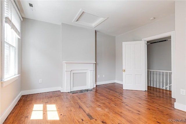 unfurnished living room with attic access, hardwood / wood-style floors, visible vents, and baseboards