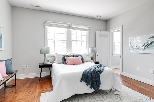 bedroom with baseboards, wood finished floors, visible vents, and multiple windows