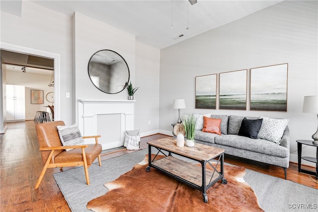living room featuring a high ceiling, wood finished floors, visible vents, baseboards, and a fireplace