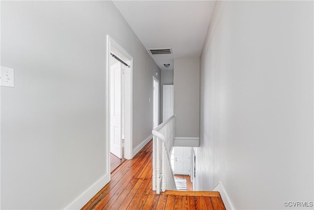 corridor featuring baseboards, hardwood / wood-style flooring, visible vents, and an upstairs landing