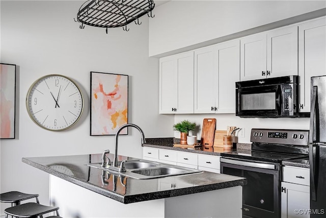 kitchen featuring dark countertops, a sink, black appliances, a kitchen bar, and white cabinetry