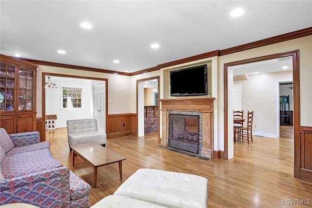living room with crown molding, light wood-style floors, recessed lighting, a high end fireplace, and a wainscoted wall