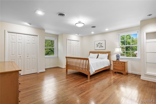 bedroom with baseboards, multiple closets, visible vents, and light wood-style floors