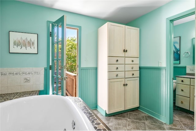full bath featuring a jetted tub, tile patterned flooring, and a wainscoted wall