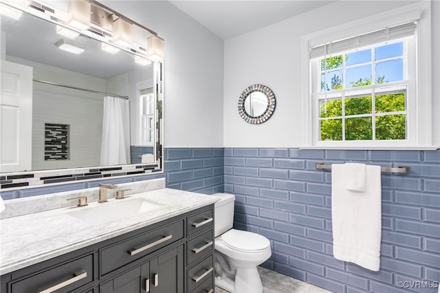 bathroom with tile walls, curtained shower, a wainscoted wall, vanity, and toilet