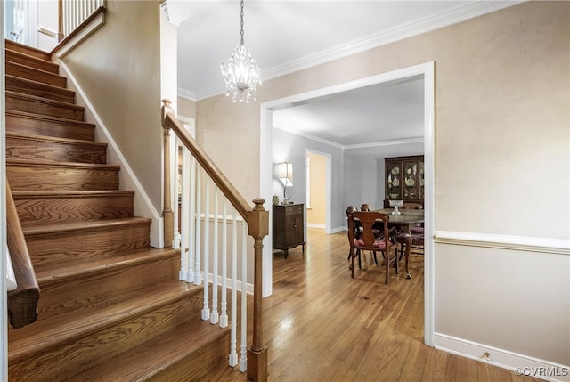 staircase featuring an inviting chandelier, baseboards, ornamental molding, and hardwood / wood-style floors