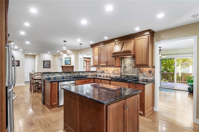 kitchen featuring backsplash, appliances with stainless steel finishes, light wood-type flooring, a sink, and a peninsula