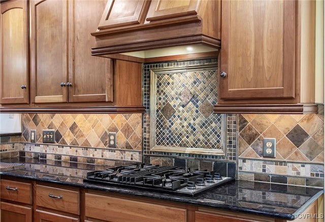 kitchen with gas cooktop, brown cabinetry, dark stone counters, custom range hood, and tasteful backsplash