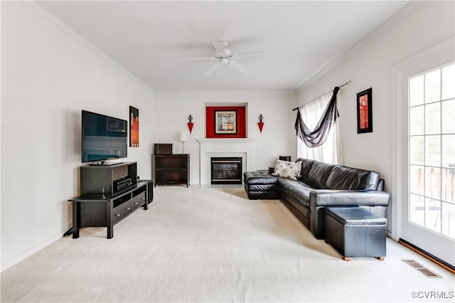 carpeted living room with crown molding, ceiling fan, a glass covered fireplace, baseboards, and visible vents