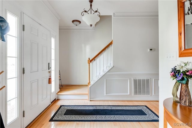 entryway featuring stairway, crown molding, wood finished floors, and visible vents