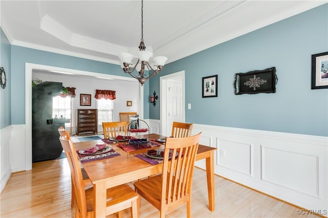 dining room with crown molding, a decorative wall, light wood-type flooring, a wainscoted wall, and a chandelier