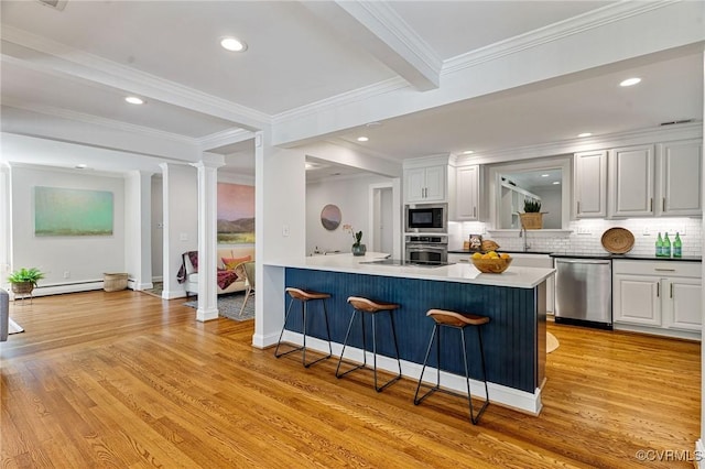 kitchen featuring stainless steel appliances, a baseboard heating unit, a breakfast bar, and light wood finished floors