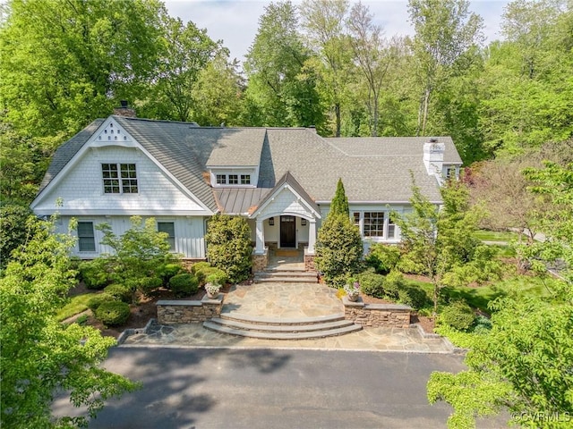 view of front of property featuring a chimney, a standing seam roof, a shingled roof, board and batten siding, and metal roof