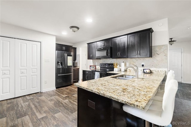kitchen featuring a peninsula, dark wood-style floors, a sink, dark cabinetry, and black appliances