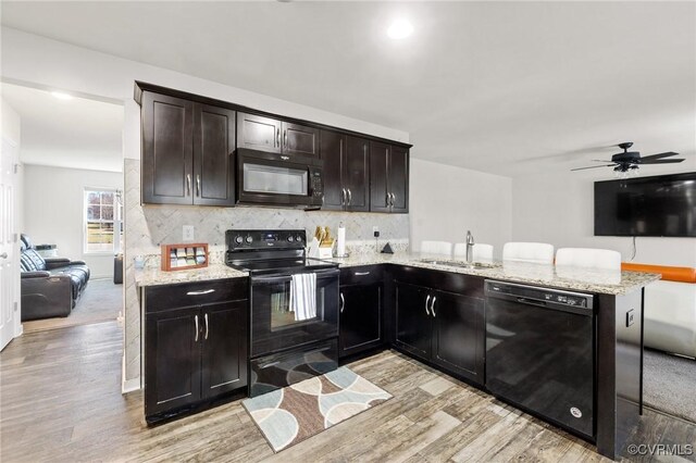 kitchen featuring light wood finished floors, open floor plan, a sink, and black appliances