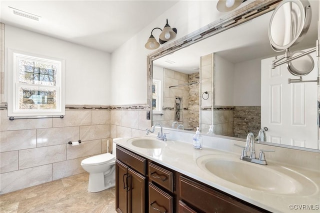 bathroom with a tile shower, visible vents, toilet, and a sink