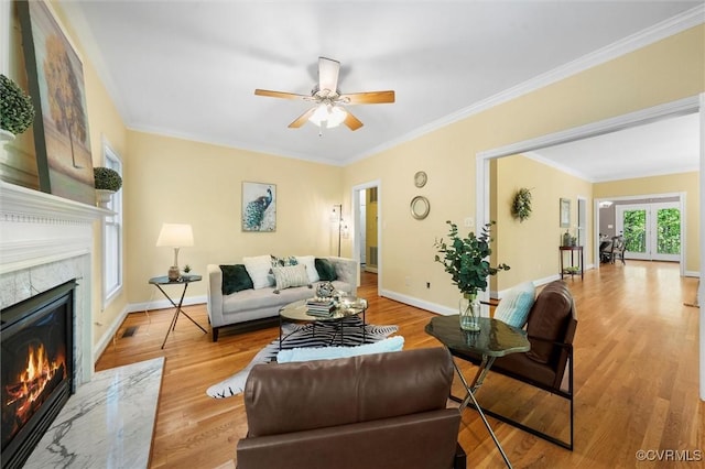 living room with ceiling fan, a high end fireplace, crown molding, wood finished floors, and baseboards
