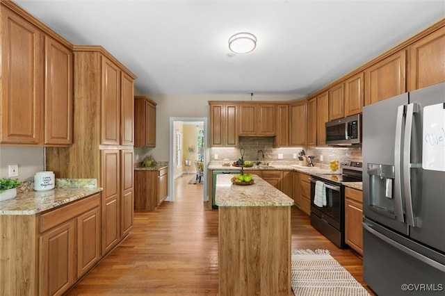 kitchen with a sink, light wood finished floors, stainless steel appliances, backsplash, and a kitchen island