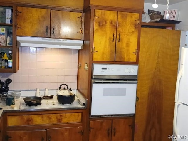 kitchen with decorative backsplash, brown cabinets, white appliances, and under cabinet range hood