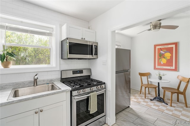 kitchen featuring stainless steel appliances, a sink, backsplash, white cabinetry, and light countertops