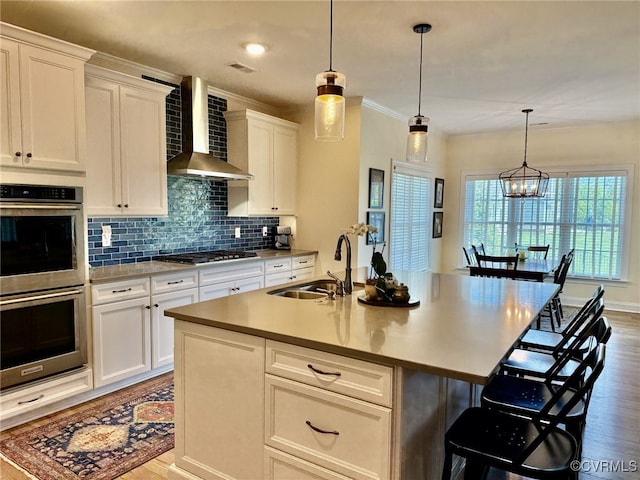 kitchen with stainless steel appliances, a sink, wall chimney exhaust hood, and wood finished floors