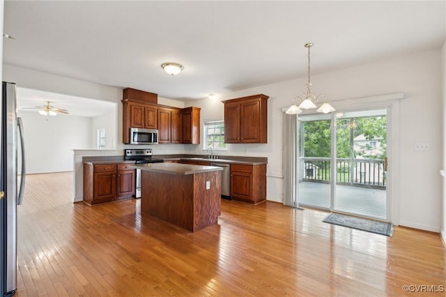 kitchen featuring dark countertops, a center island, a sink, light wood-style flooring, and stainless steel appliances