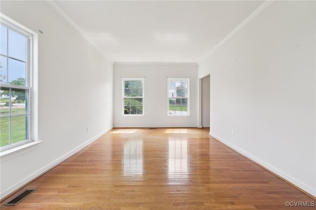 spare room featuring baseboards, ornamental molding, light wood finished floors, and visible vents