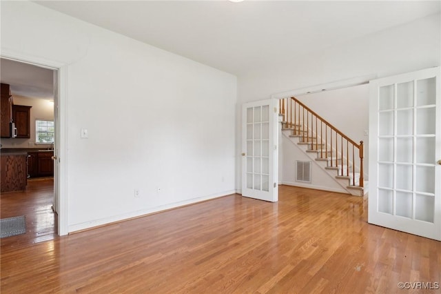 unfurnished living room with visible vents, baseboards, stairway, french doors, and light wood finished floors