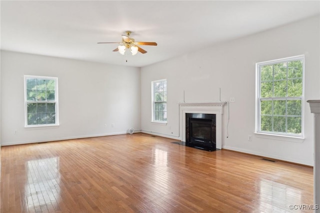 unfurnished living room with ceiling fan, a fireplace with flush hearth, a wealth of natural light, and visible vents