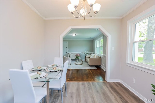 dining space with arched walkways, wood finished floors, ornamental molding, and a notable chandelier