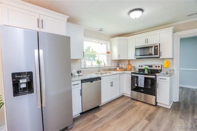 kitchen with a sink, light wood-style floors, appliances with stainless steel finishes, white cabinets, and ornamental molding