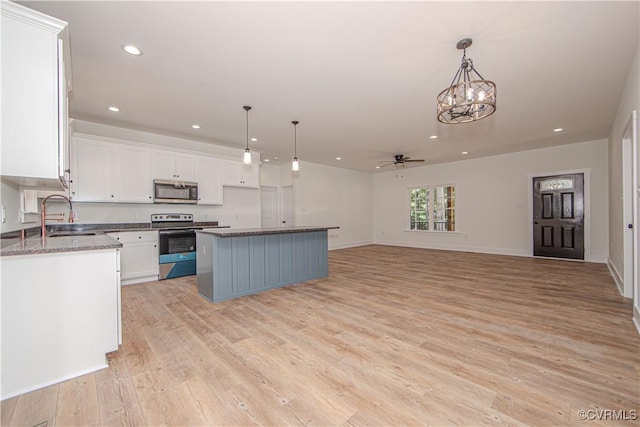 kitchen with white cabinets, light wood-type flooring, ceiling fan with notable chandelier, appliances with stainless steel finishes, and hanging light fixtures