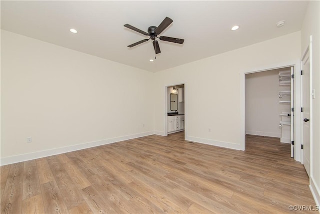 unfurnished bedroom with recessed lighting, a spacious closet, connected bathroom, baseboards, and light wood-style flooring