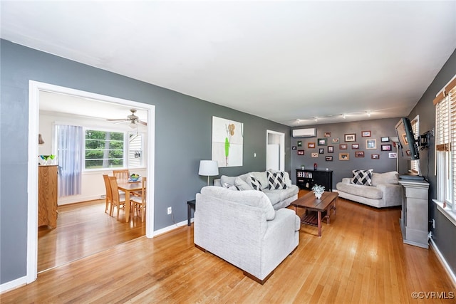 living room featuring baseboards, ceiling fan, a wall mounted AC, and light wood-style flooring
