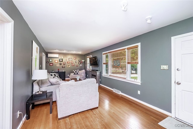 living area with baseboards, a wall unit AC, wood finished floors, and visible vents