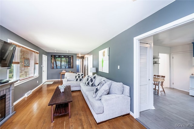 living area with baseboards, visible vents, wood finished floors, and a fireplace
