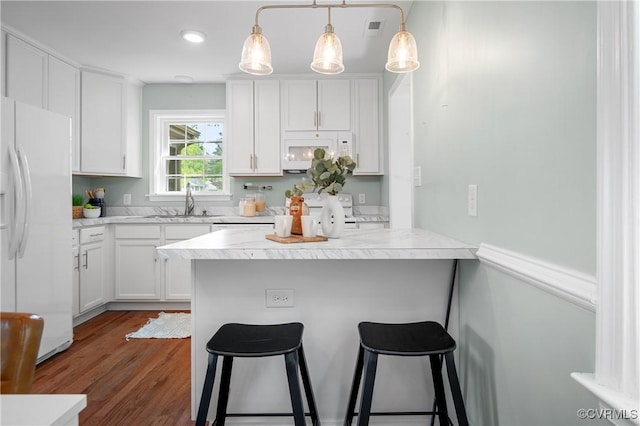 kitchen with white cabinets, a sink, white appliances, light countertops, and a breakfast bar area