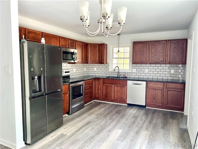 kitchen featuring dark countertops, a sink, a chandelier, light wood-style floors, and stainless steel appliances
