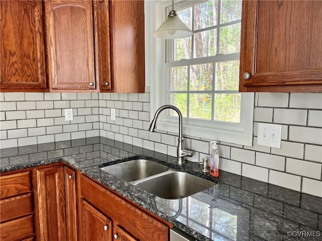 kitchen featuring a sink, dark stone countertops, decorative backsplash, brown cabinets, and hanging light fixtures