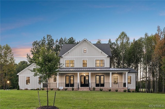 back of house at dusk featuring a standing seam roof, metal roof, covered porch, a lawn, and board and batten siding