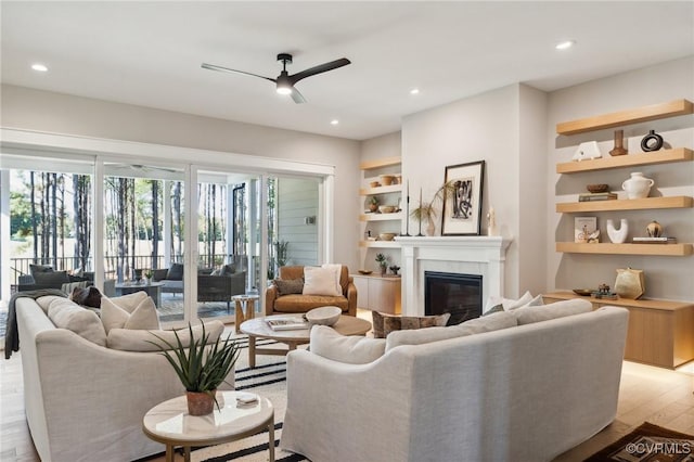 living room with a glass covered fireplace, recessed lighting, light wood-style floors, built in shelves, and a ceiling fan
