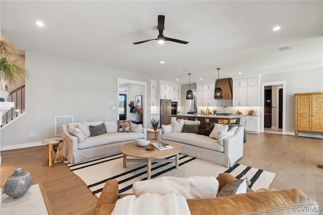 living room with light wood-type flooring, visible vents, recessed lighting, a ceiling fan, and stairs