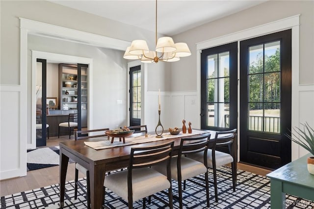dining room with light wood finished floors, a wainscoted wall, a chandelier, and a decorative wall